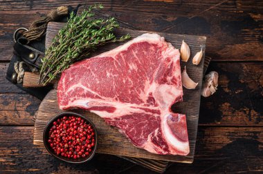 Biftekli biftek, kasap panosunda çiğ biftek ve şifalı otlar. Ahşap arka plan. Üst görünüm.