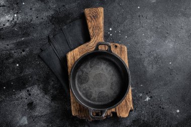 Cooking background with Empty cast-iron skillet on rustic towel. Black background. Top view. Copy space.