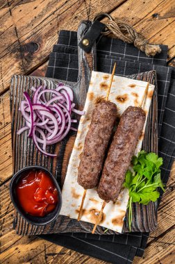 Traditional middle east kefta, kofta kebab from ground beef and lamb meat grilled on skewers served with flatbread and onion. Wooden background. Top view.
