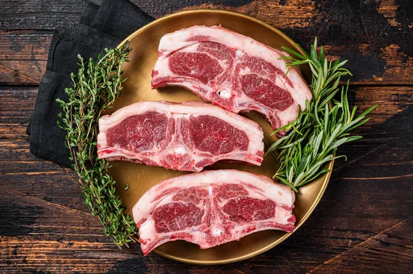 Uncooked Raw lamb loin chops steaks, saddle in plate with rosemary and thyme. Wooden background. Top view.