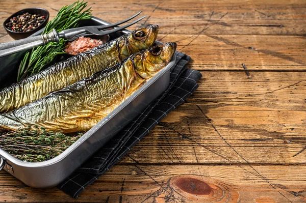 Smoked marinated herring fish in kitchen tray with herbs. Wooden background. Top view. Copy space.