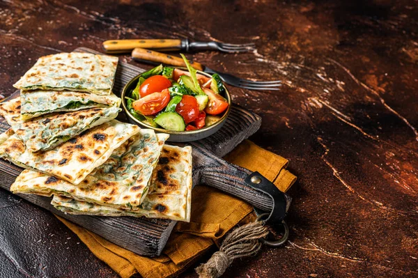 Freshly baked Turkish Gozleme, flatbread with greens and cheese. Dark background. Top view. Copy space.