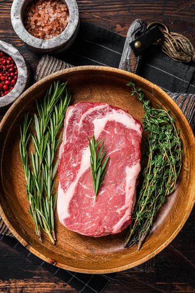 Rib-eye raw Steak, rib eye beef marbled meat in wooden plate with rosemary and thyme. Wooden background. Top view.