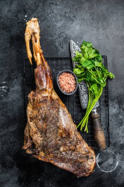 BBQ Roasted lamb mutton leg with herbs and spices on a grill. Black background. Top view.