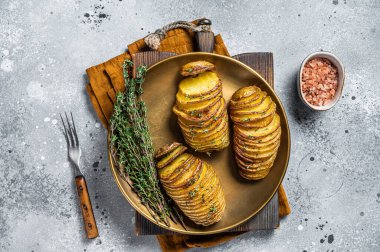 Baked Hasselback Potato with Fresh thyme and rosemary. Gray background. Top view.