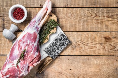 Butcher board with Raw lamb mutton leg with herbs. Wooden background. Top view. Copy space.