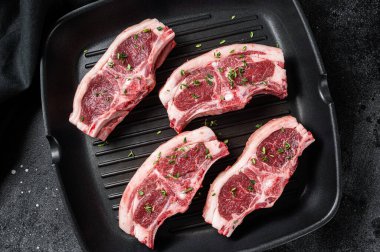 Raw lamb loin rib chops steaks in grill skillet with rosemary and thyme. Black background. Top view.