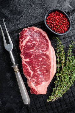 Raw striploin or New York beef meat steak ready for BBQ. Black background. Top view.