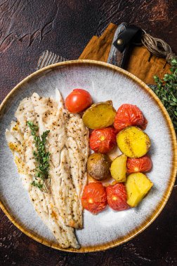 Kavrulmuş Pollock balığı filetosu, garnitür domates ve patatesle birlikte tabakta. Karanlık arka plan. Üst görünüm.