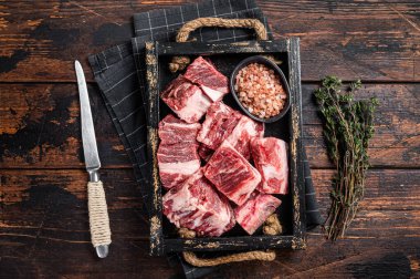 Uncooked Raw diced cubes of lamb meat in wooden tray with salt and thyme. Wooden background. Top view.