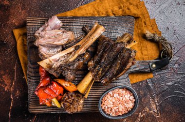 Traditionally slow cooked Leg of Lamb or Lamb Shank with vegetables on a cutting board. Dark background. Top view.