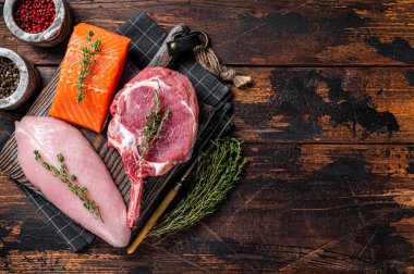 Raw steaks - fish salmon, beef meat and turkey breast fillet on a cutting board. Wooden background. Top view. Copy space.
