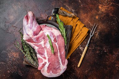 Mutton lamb whole shoulder, raw meat in a steel tray with herbs. Dark background. Top view.