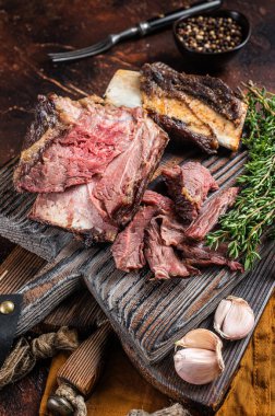 Tahta kesme tahtasında kekik ile ağır ateşte pişmiş dana eti. Karanlık arka plan. Üst görünüm.