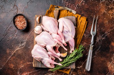 Plucked raw quails, fresh poultry on wooden board with spices. Dark background. Top view.