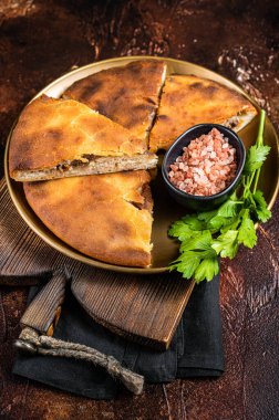 Traditional Ossetian pie sliced on a plate. Dark background. Top view.