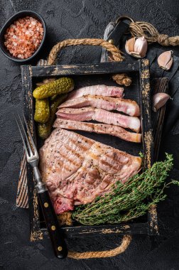 Ahşap tepside otlarla pişirilmiş ızgara domuz bifteği. Siyah arka plan. Üst görünüm.