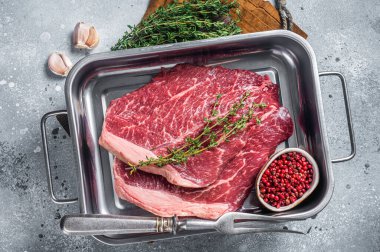 Mutfak tepsisinde baharatlı ince mermer biftek. Gri arka plan. Üst görünüm.