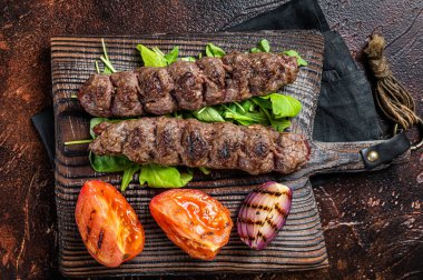 Turkish adana kebab, ground beef and lamb meat grilled on skewers served with tomato, salad and onion. Dark background. Top view.