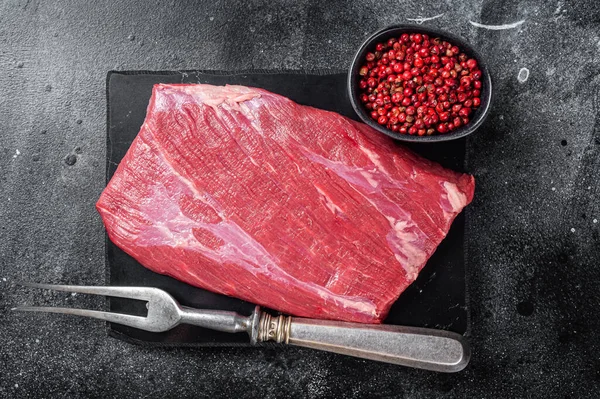 Prime choice flank steak, raw beef meat on marble board with herbs. Black background. Top view.