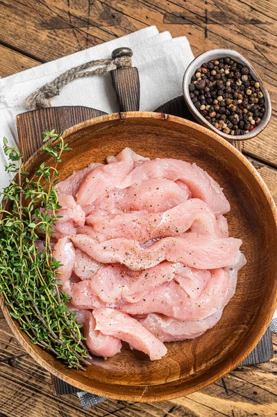 Sliced raw chicken, turkey breast meat in a wooden plate with thyme. Wooden background. Top view.