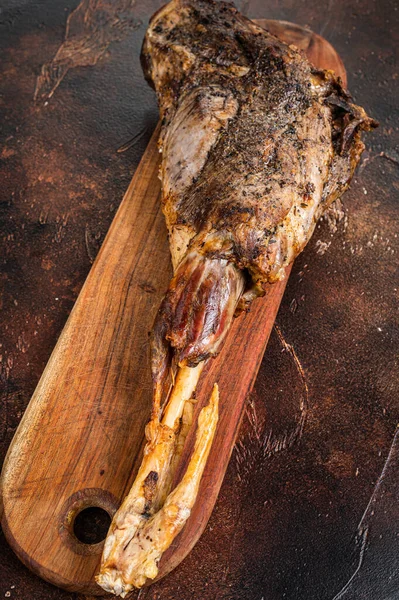 Roast lamb leg meat with herbs and spices on a cutting board. Dark background. Top view.