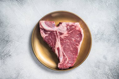 Altın metal tabakta çiğ biftek biftek bifteği. Gri arka plan. Üst görünüm.