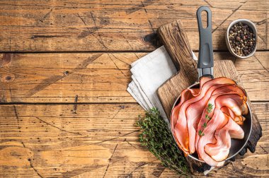 Thinly sliced German Black Forest Ham bacon in skillet. Wooden background. Top view. Copy space.