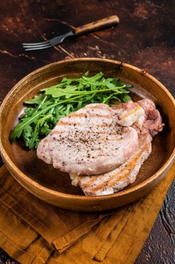 Roasted pork chop steaks or cutlets with arugula salad. Dark background. Top view.