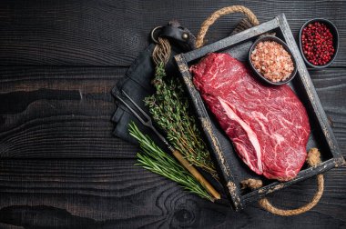 Unccoked rump steak or raw top sirloin beef meat steak. Black wooden background. Top view. Copy space.