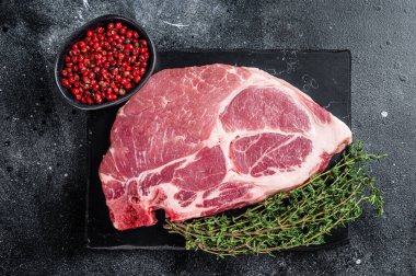 Mermer tahtada çiğ etten yapılmış domuz boyunlu biftek ve otlar. Siyah arka plan. Üst görünüm.