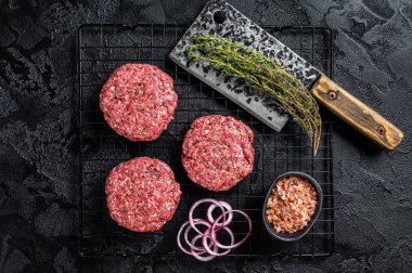 Raw minced beef cutlets with spices and herbs ready for cooking. Black background. Top view.