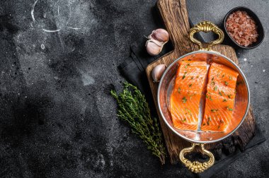 Uncooked Salmon fillet steaks, raw organic fish in skillet ready for cooking. Black background. Top view. Copy space.