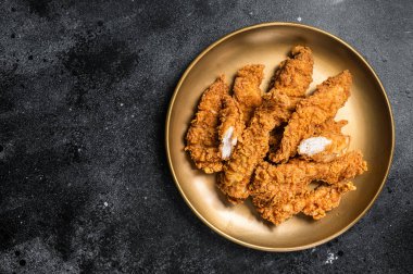 Breaded chicken strips, breast fillet meat on a plate. Black backgrund. Top view. Copy space.
