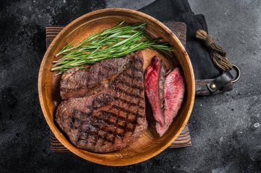 Barbekü ızgara orta pişmiş sığır filetosu bifteği, ahşap tabakta biftek. Siyah arka plan. Üst görünüm.