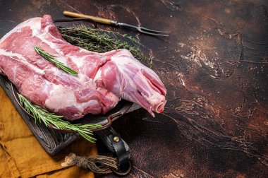 Mutton lamb whole shoulder, raw meat in a steel tray with herbs. Dark background. Top view. Copy space.