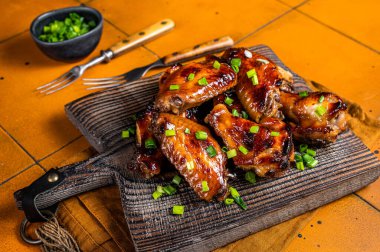 Grilled sweet and sour chicken wings on wooden board. Orange background. Top view.