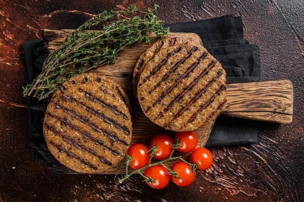 BBQ Grilled plant based meat burger patties, vegan cutlets on wooden board with herbs. Dark background. Top view.
