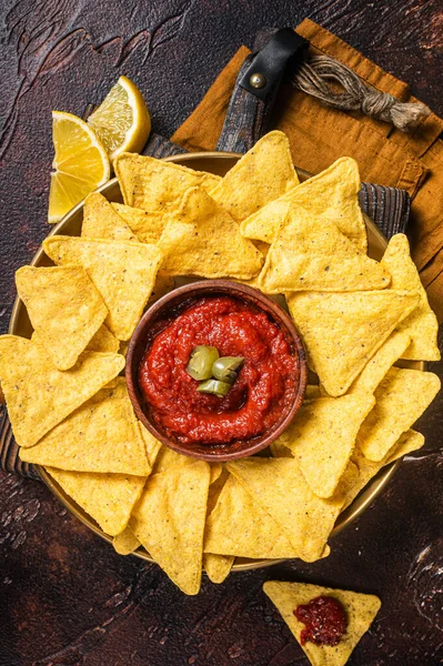 Nachos chips with tomato sauce and jalapeno, mexican appetizer. Dark background. Top view.