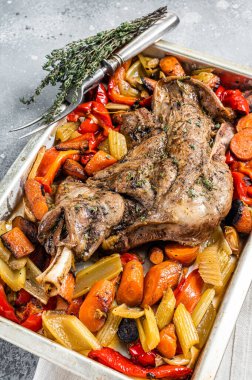 Roast lamb mutton shoulder meat in a baking dish with vegetables. Gray background. Top view.