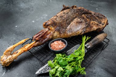 BBQ Roasted lamb mutton leg with herbs and spices on a grill. Black background. Top view.