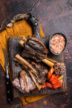 Traditionally slow cooked Leg of Lamb or Lamb Shank with vegetables on a cutting board. Dark background. Top view.