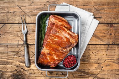 American Smoked Pork spare Ribs in steel tray with herbs. Wooden background. Top view.