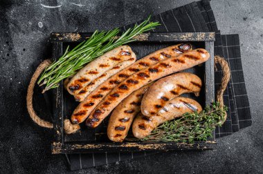 Fried on a grill skillet mix sausages in a wooden tray with herbs. Black background. Top view.