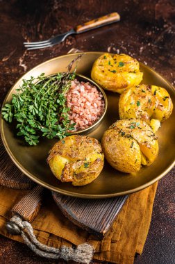 Crushed, smashed potatoes baked with rosemary and thyme on plate. Dark background. Top view.