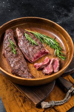 Fried sirloin flap or flank beef steak with herbs in a wooden plate. Black background. Top view.