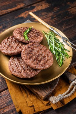 Grilled burger beef meat patty with herbs and spices on steel plate. Wooden background. Top view.