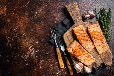 Grilled salmon fillets, fish steaks on wooden board with thyme. Dark background. Top view. Copy space.