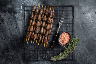 Grilled shish kebab with chicken hearts on a grill. Black background. Top view.