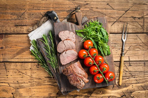 Kızarmış dana filetosu, ahşap tahtada dilimlenmiş biftek ve garnitür. Ahşap arka plan. Üst görünüm.
